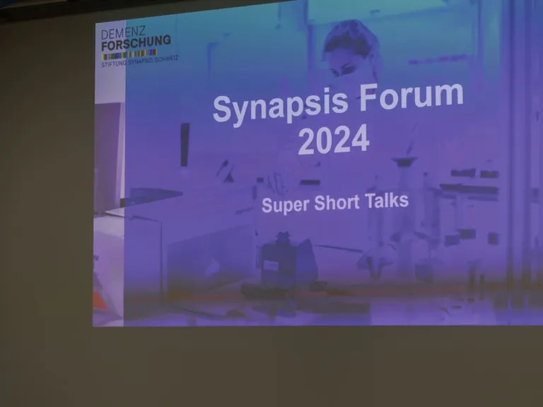 Powerpoint presentation with title of Synapsis Forum slide projected onto the wall.